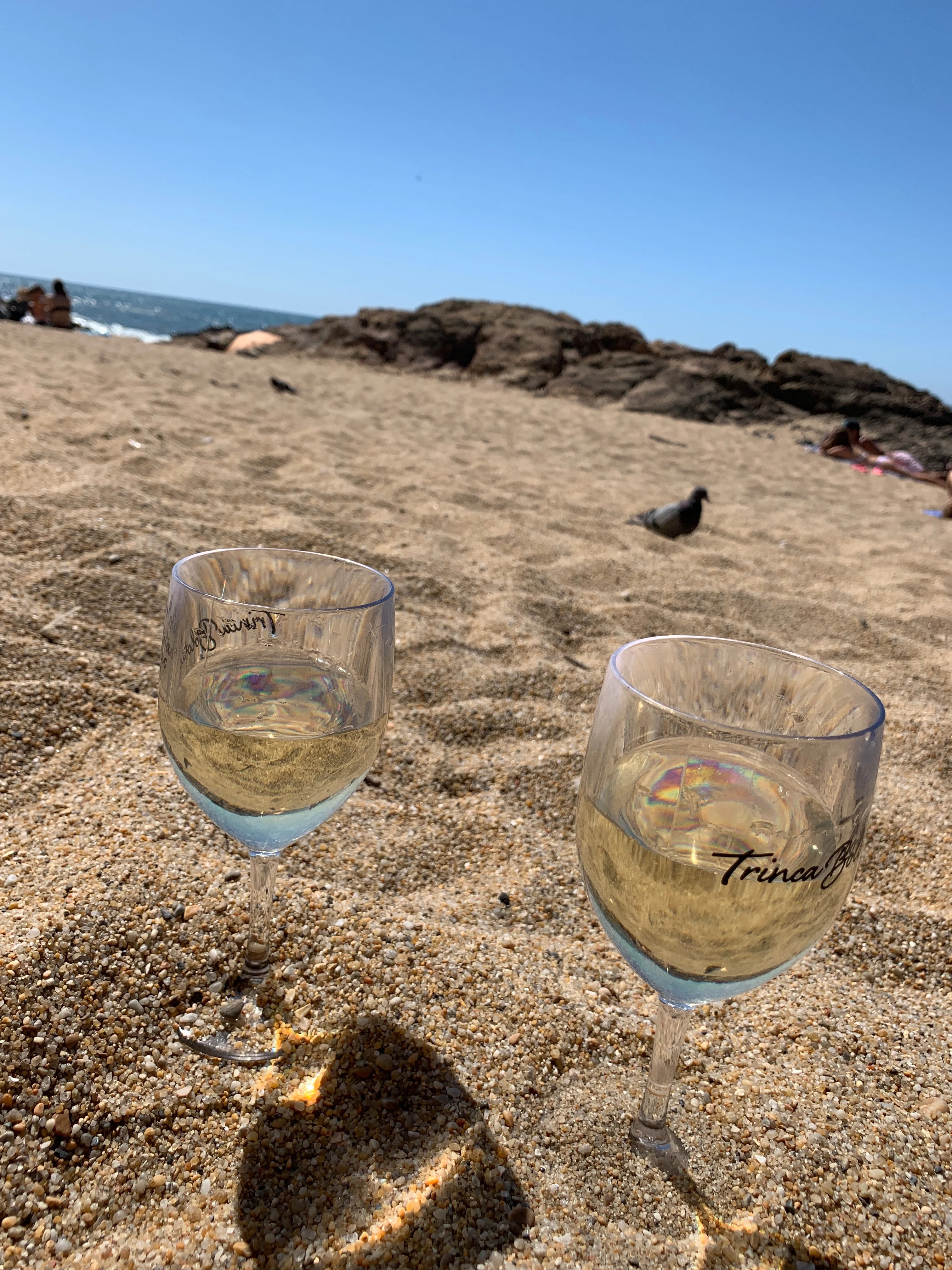 Two glasses of white wine in the sand with the ocean in the background at Praia Ingleses