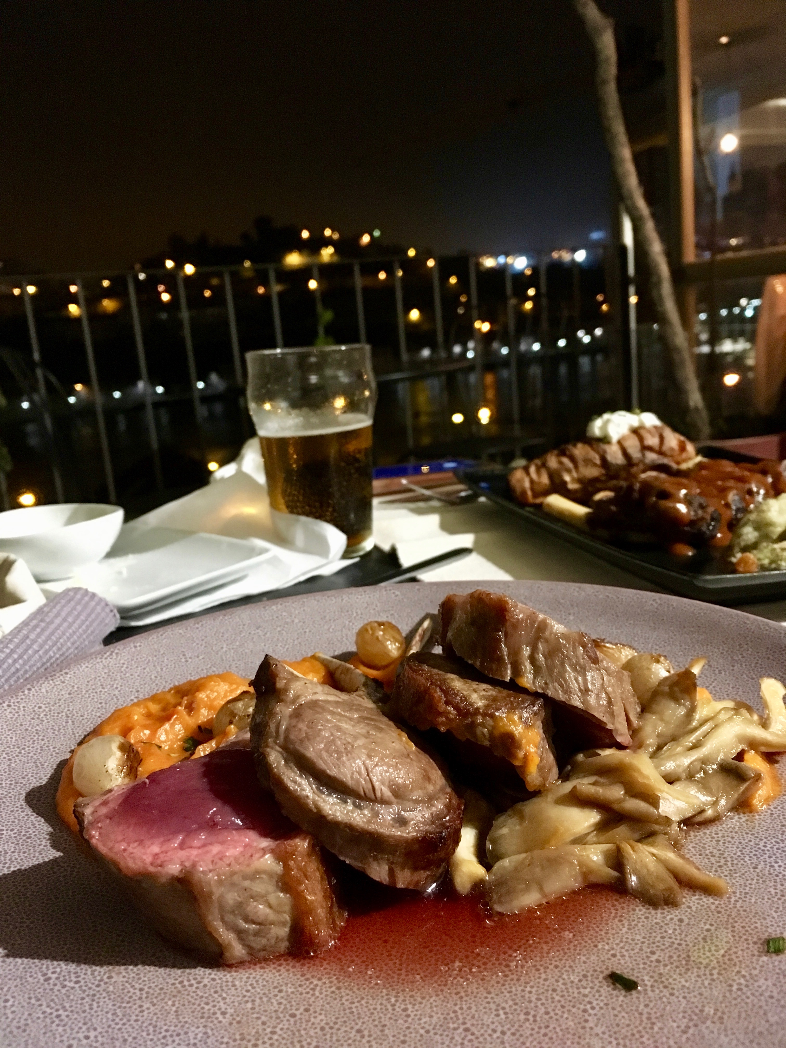 Sweet potato puree, lamb chops, and mushrooms with the city at night in the background at Intrigo