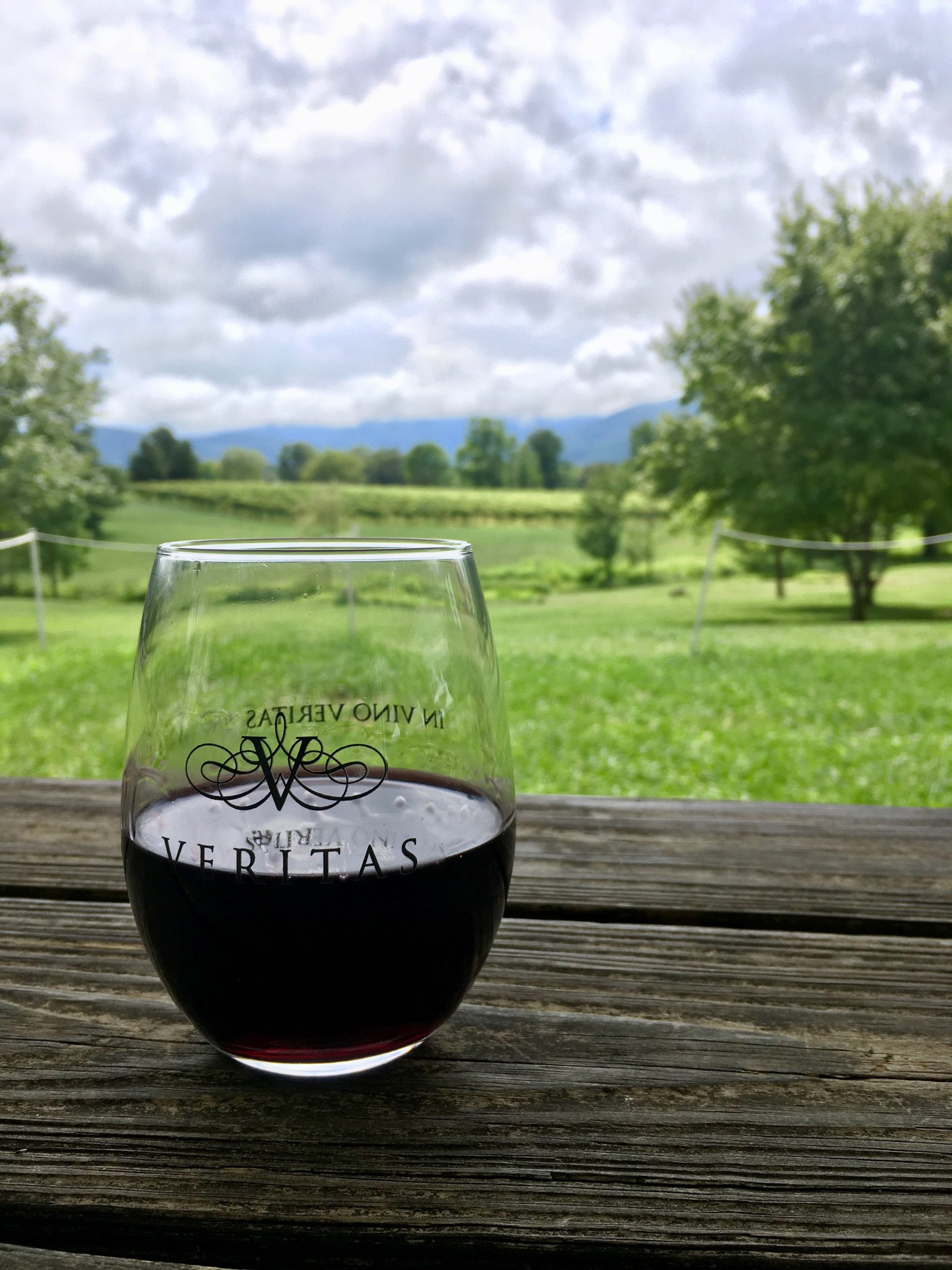 A glass of red wine on a picnic table with green vineyards in the background at Veritas Vineyards