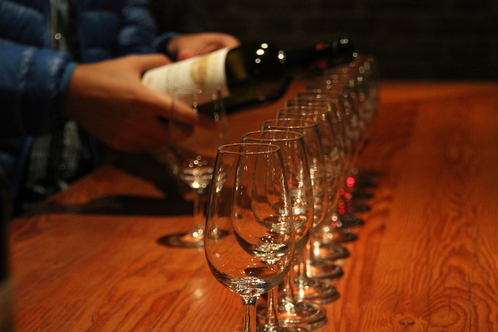 Wine being poured in a row of glasses on a wooden bar