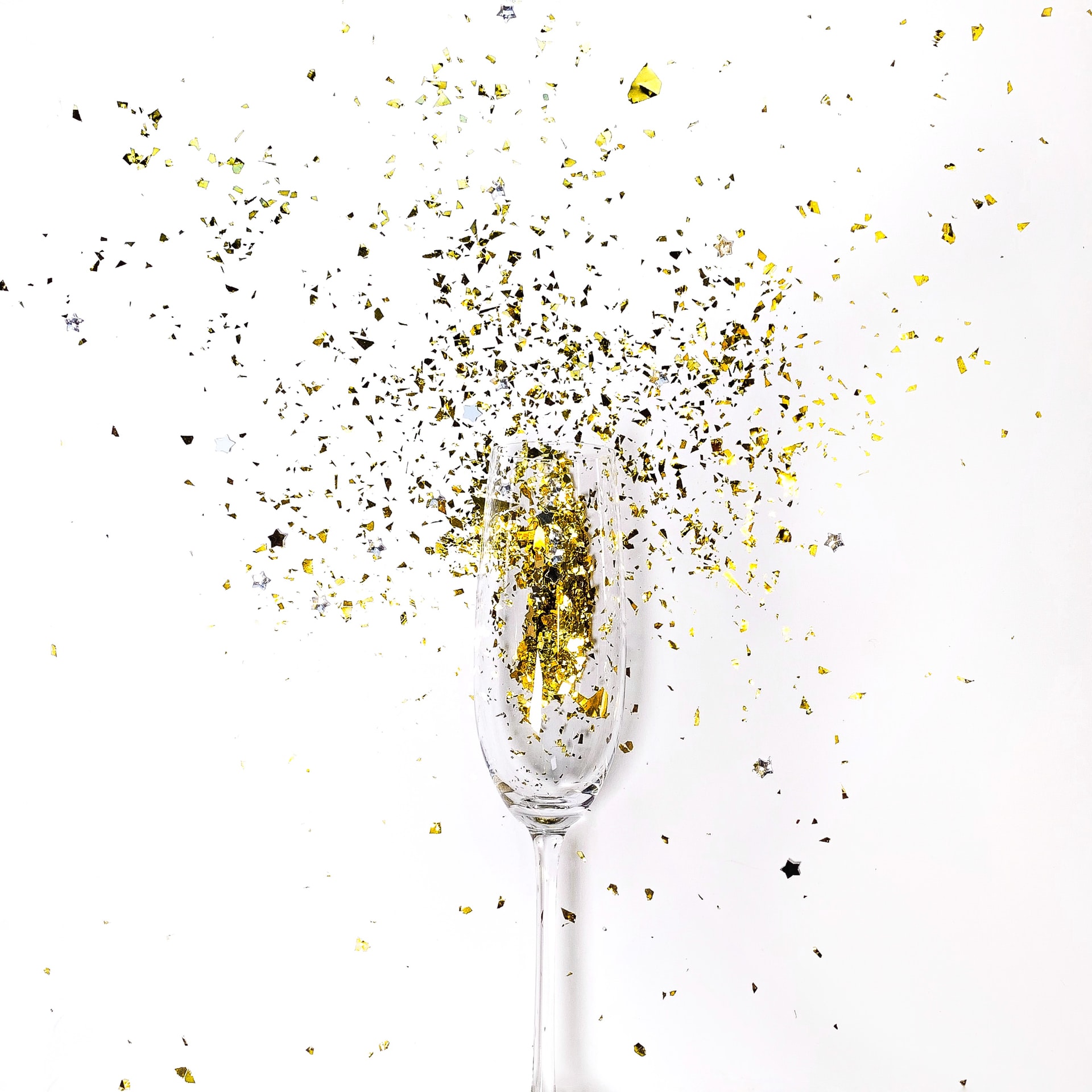 A champagne flute exploding with gold glitter on a white background.