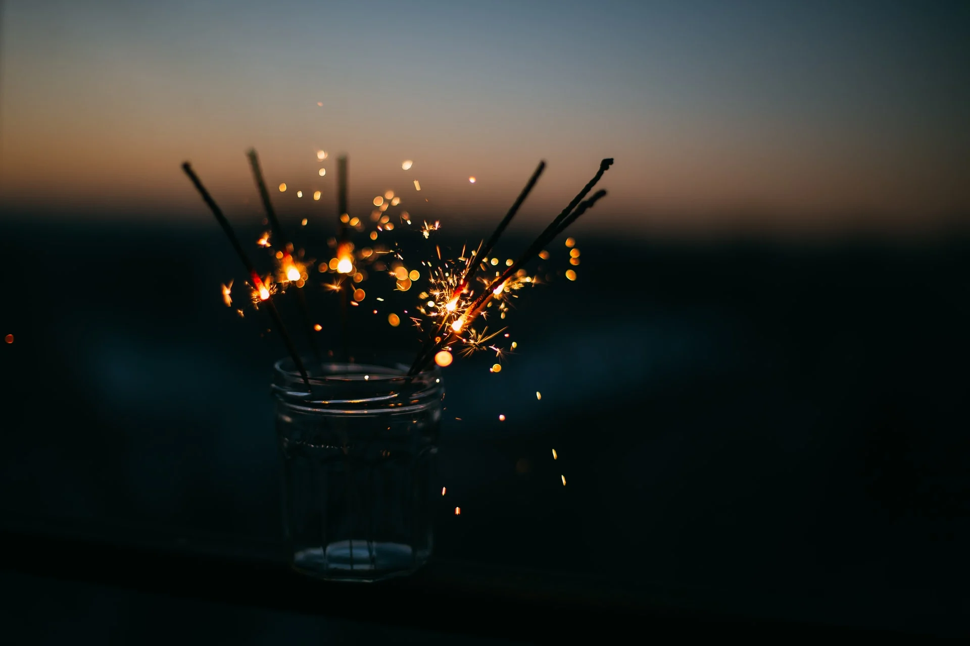 Lit sparklers glitter in a glass against a dark background.