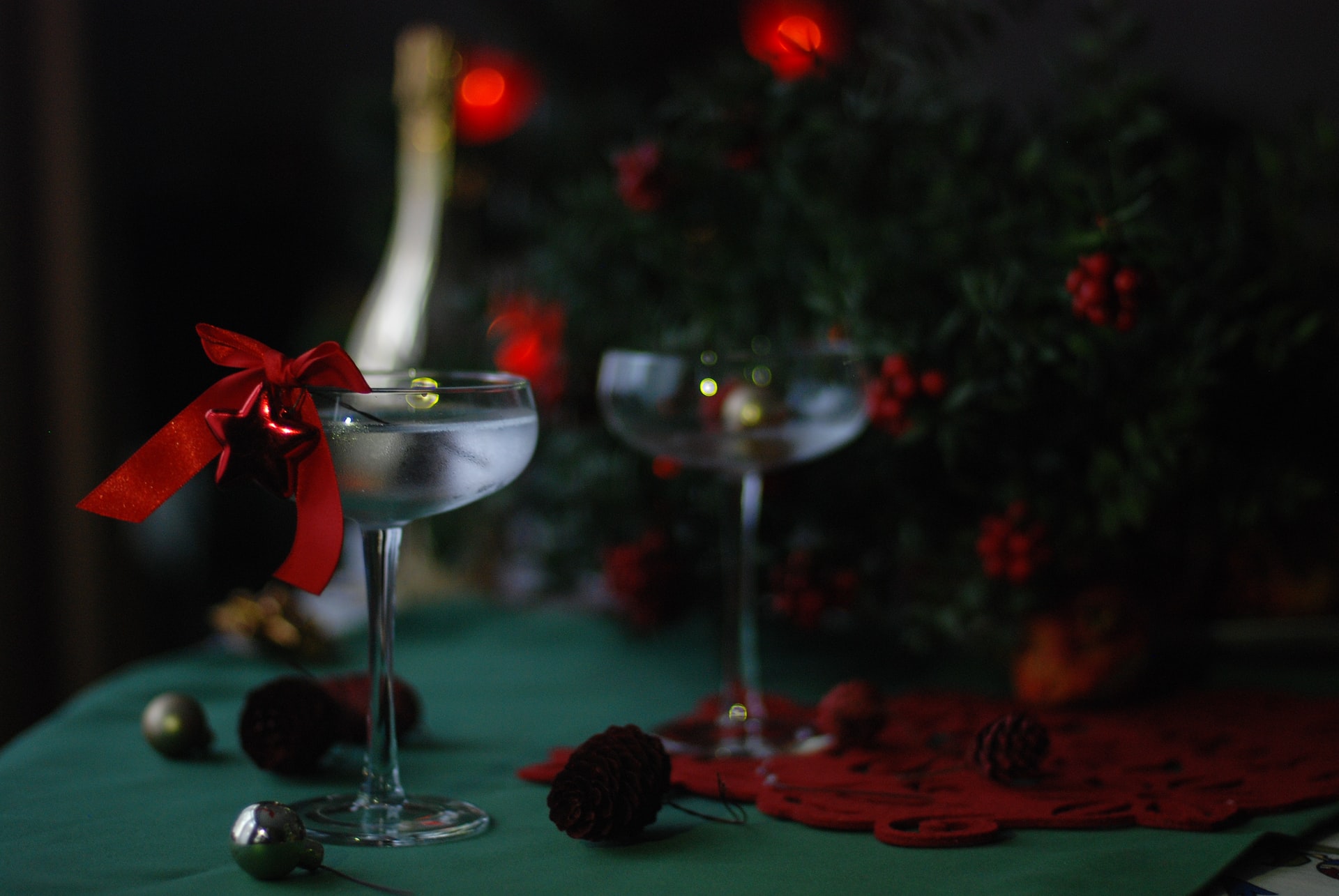 Two martinis sit in front of a Christmas tree with red ornaments.