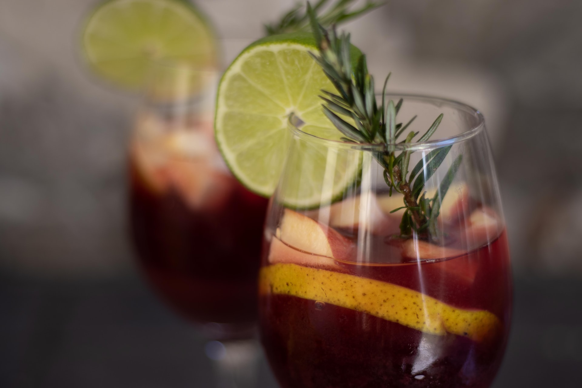 A glass of winter red sangria with apple, orange, lime, and a sprig of rosemary.