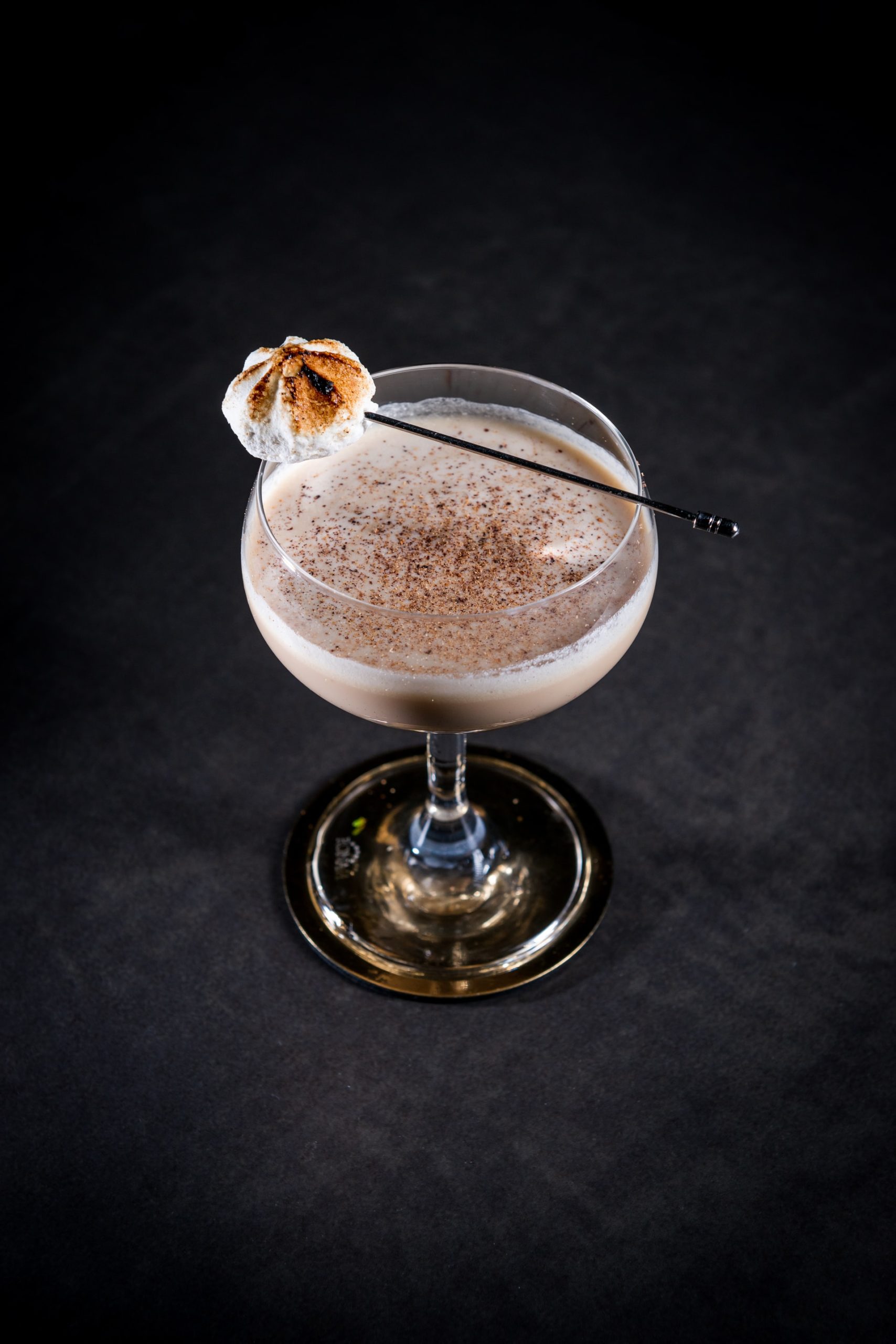 A creamy Cinnamon Toast Crunch cocktail in a coup glass with a toasted marshmallow on a skewer and sprinkle of cinnamon on top