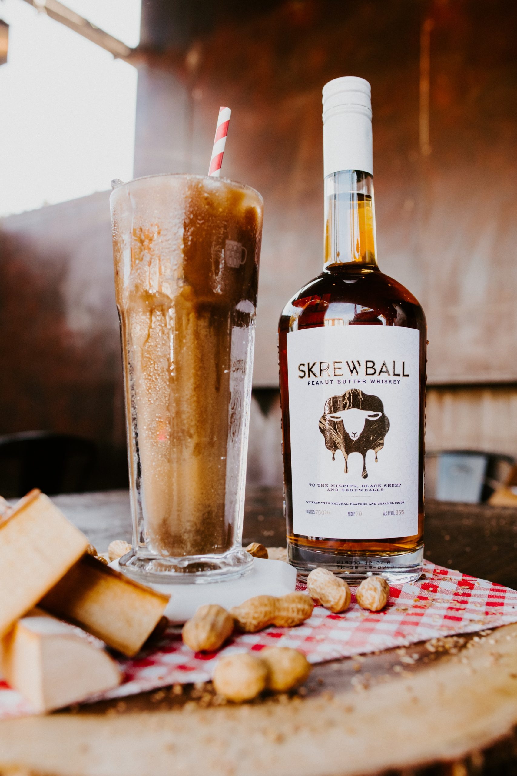 A bottle of Skrewball peanut butter whiskey next to an iced chocolate peanut butter cocktail in a tall glass.
