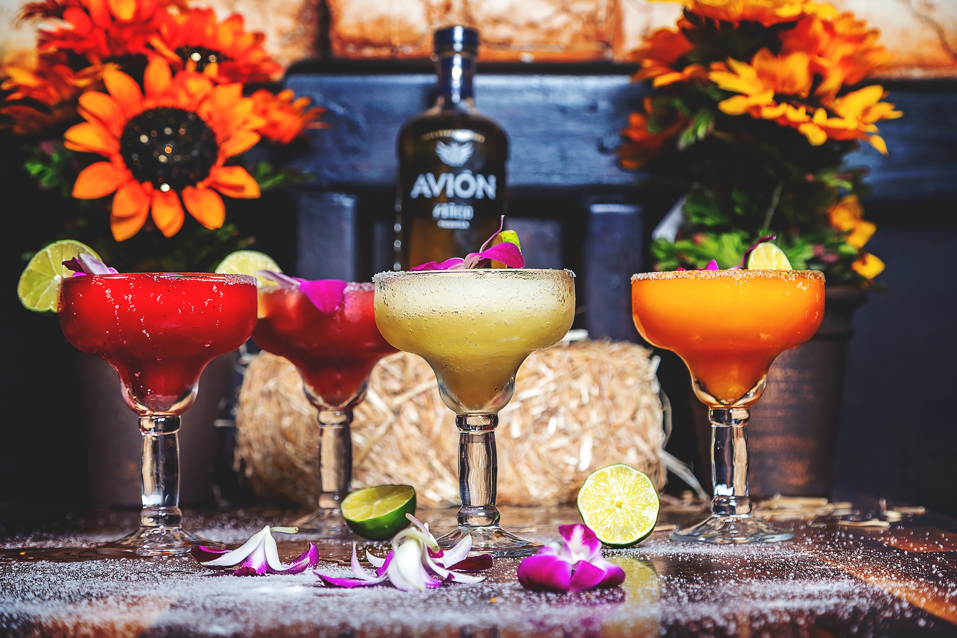 Four colorful frozen margaritas on a table with flowers in the background.