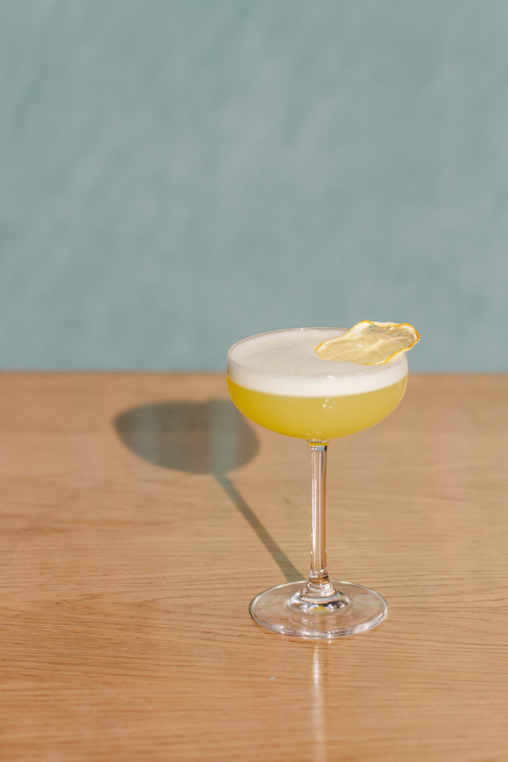 A yellow cocktail made with Yellow Chartreuse with a dried lemon garnish on a wooden table