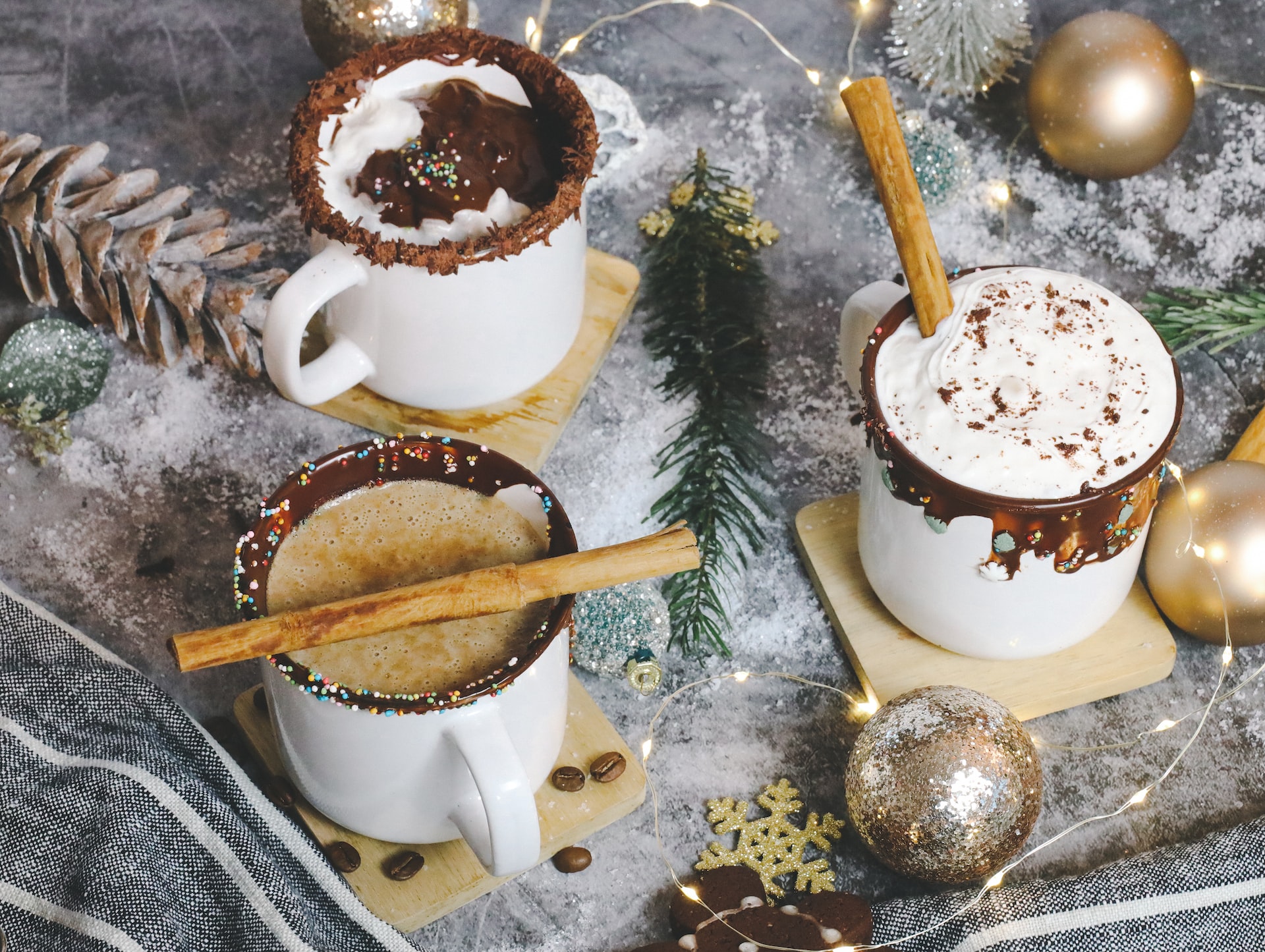 3 mugs of spiked hot chocolate with cinnamon sticks surrounded by ornaments.