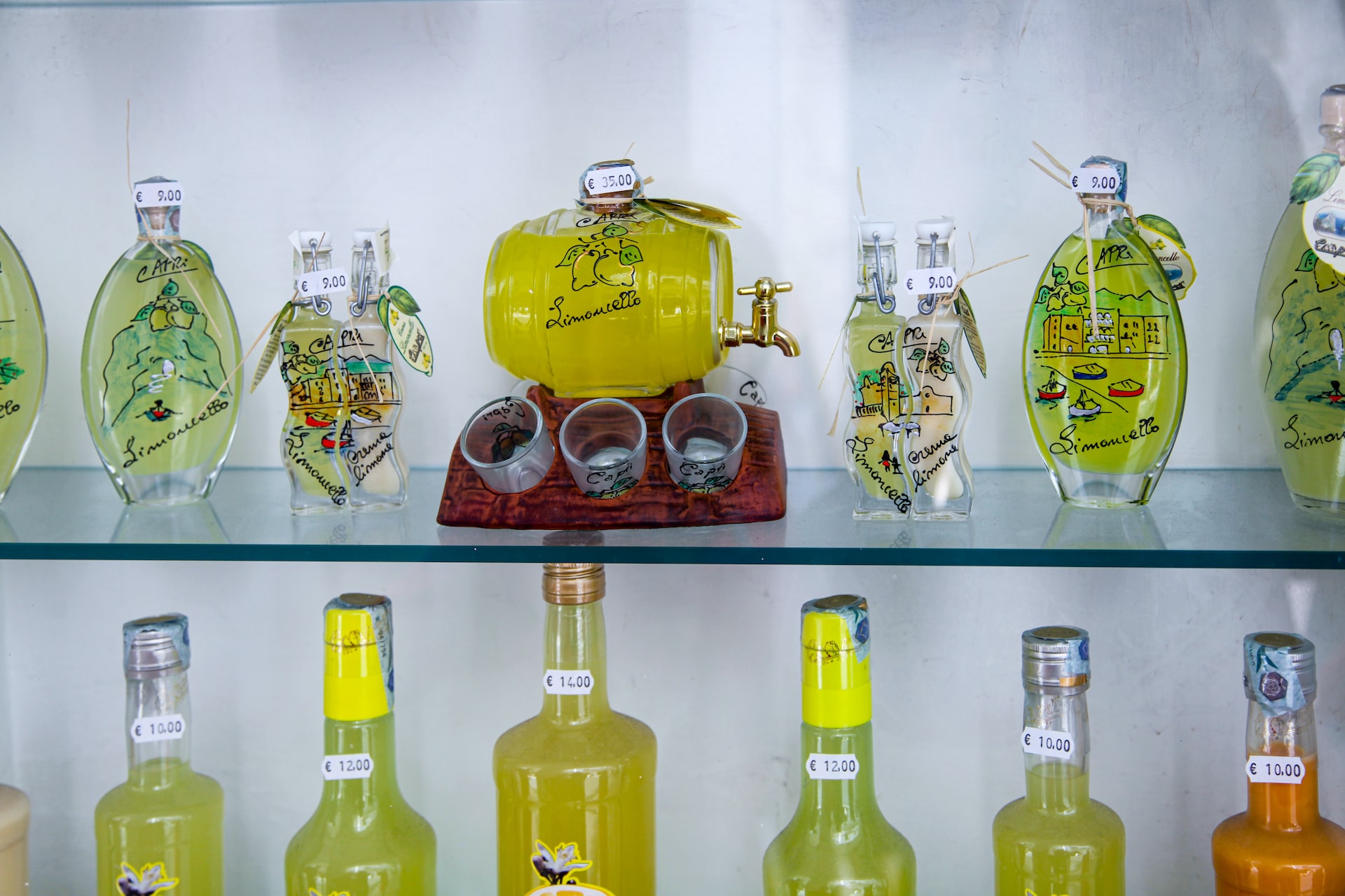 Various bottles of bright yellow limoncello with fun designs on a shelf.