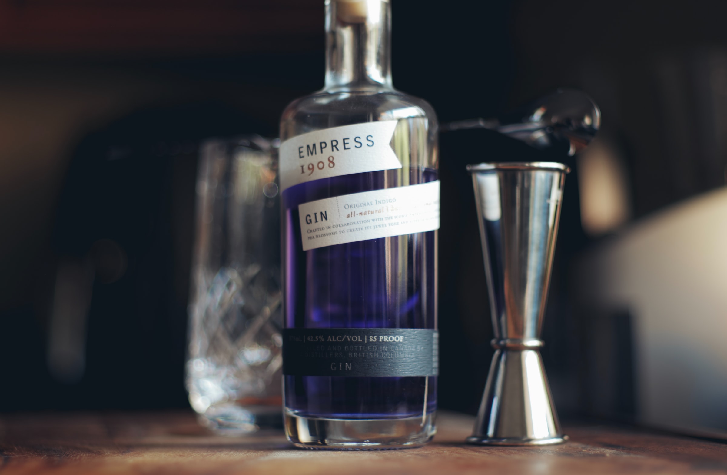 A bottle of Empress Gin on a table with a jigger and cocktail glass.