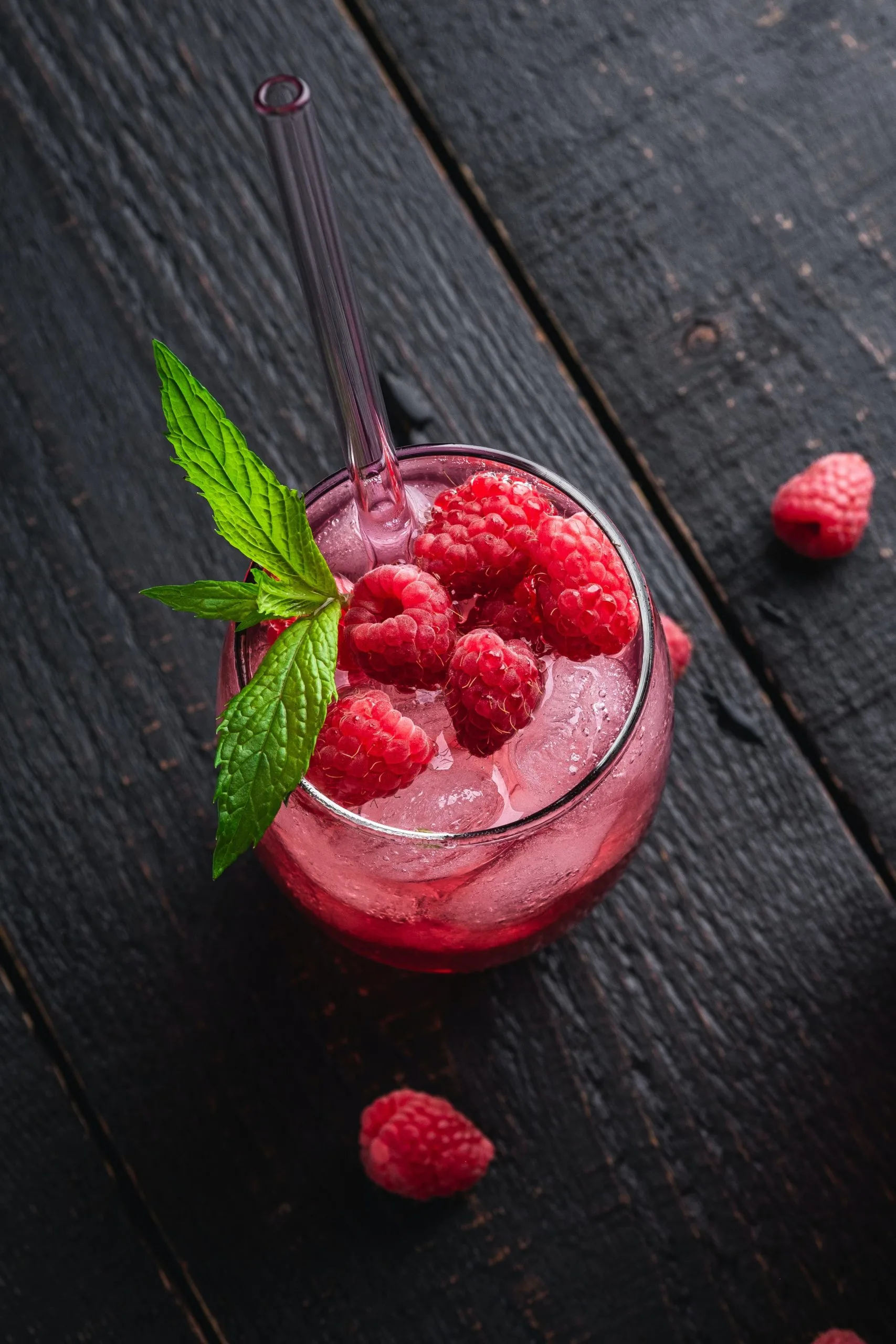 An aerial view of a Chambord Bramble cocktail on a wooden table garnished with raspberries and a sprig of mint.