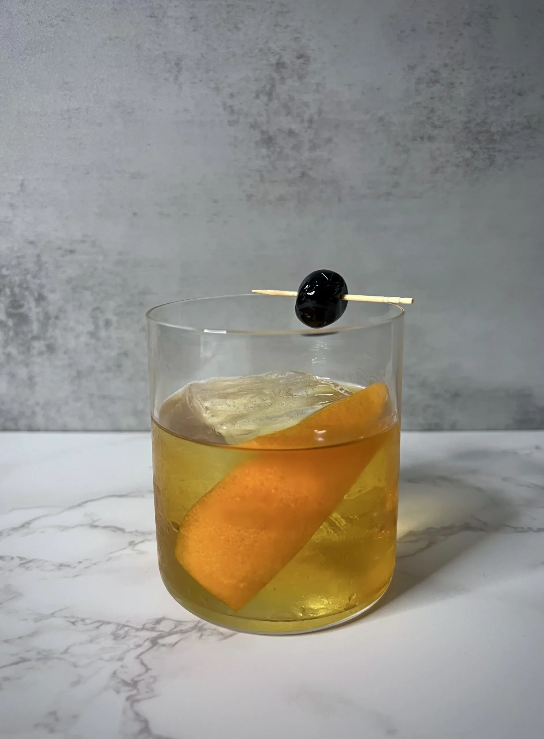 A Drambuie Old Fashioned with an orange peel and Luxardo cherry on a countertop.