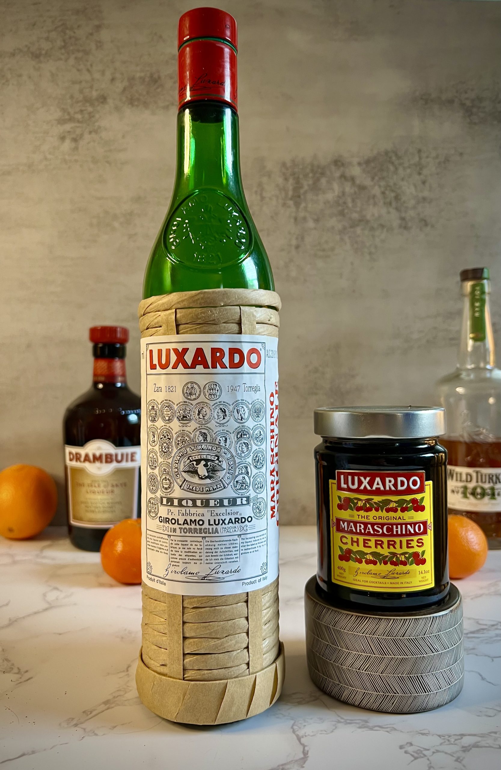 A close up of a bottle of Luxardo Maraschino Originale and Luxardo cherries on a countertop.