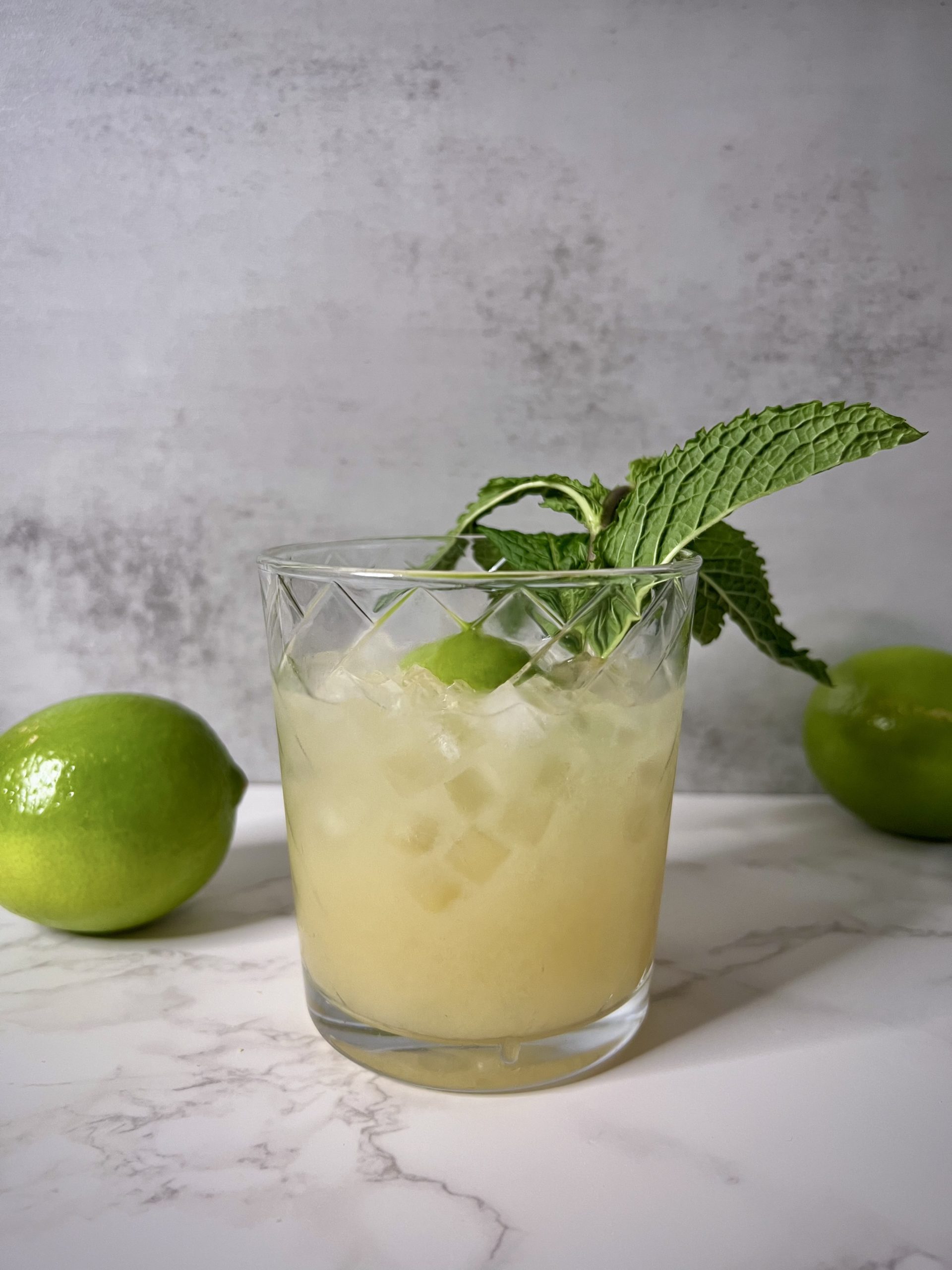 A Mai Tai on a countertop with limes in the background.