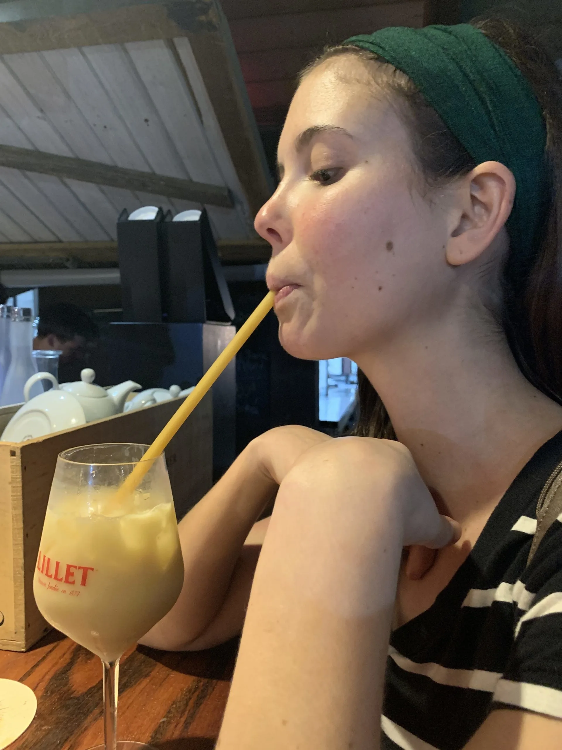 A girl drinking a Mai Tai with a long pasta tube as a straw.