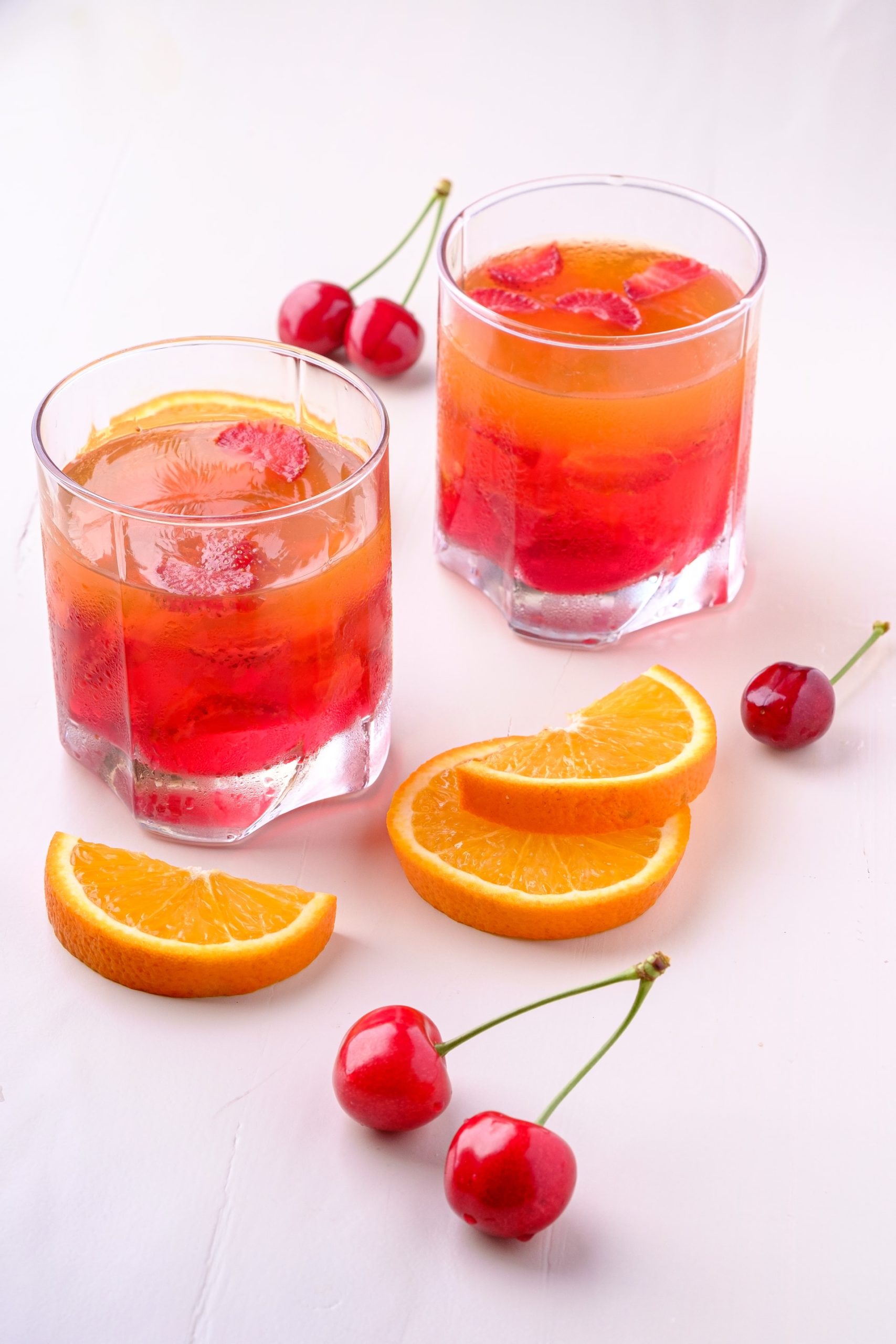 Two red and orange layered Campfire Fireball cocktails against a white background surrounded by orange slices and cherries.