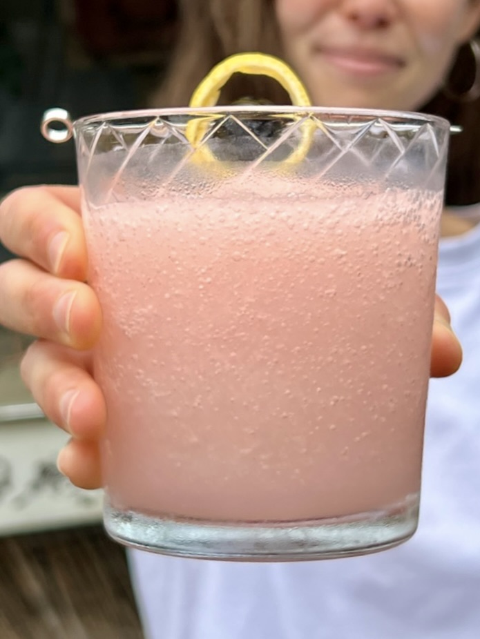 A close up shot of a light pink, frozen Saturn held in front of a blurred out smiling woman in the background.