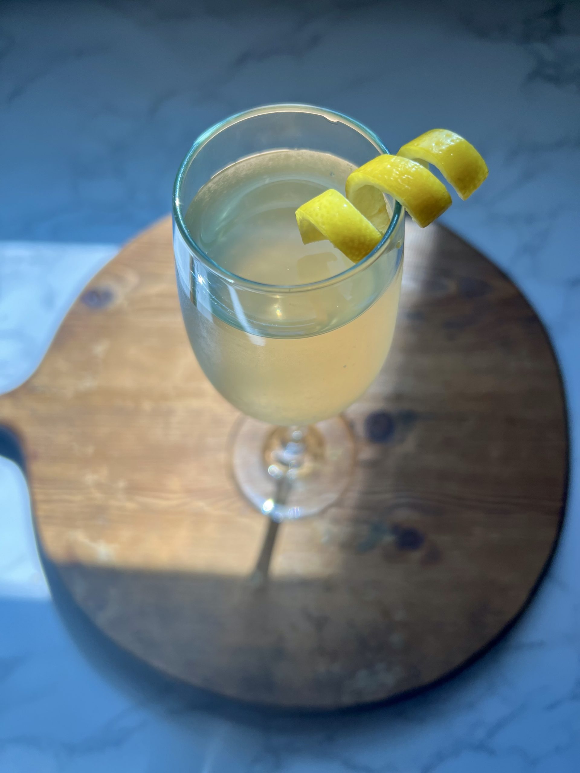 A glass of sparkling wine garnished with a lemon twist on a cutting board.