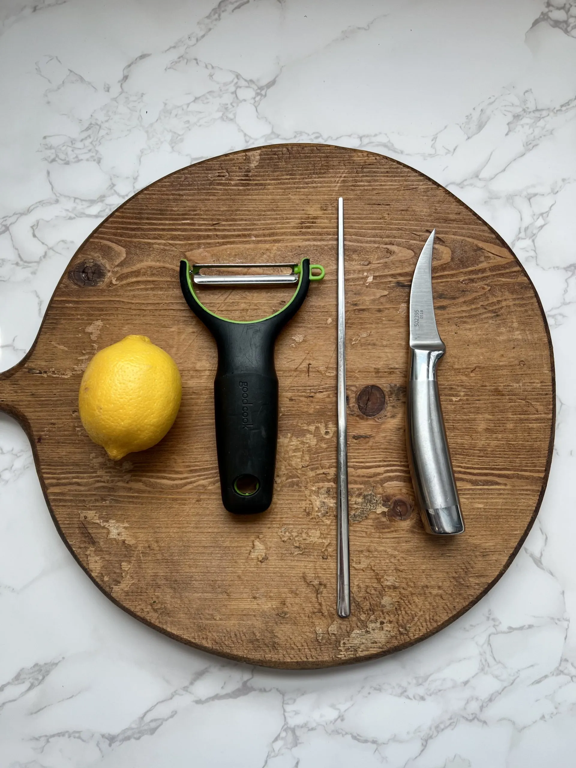 Tools needed to make a citrus twist garnish, including a ripe lemon, cutting board, vegetable peeler, chopstick, and knife.