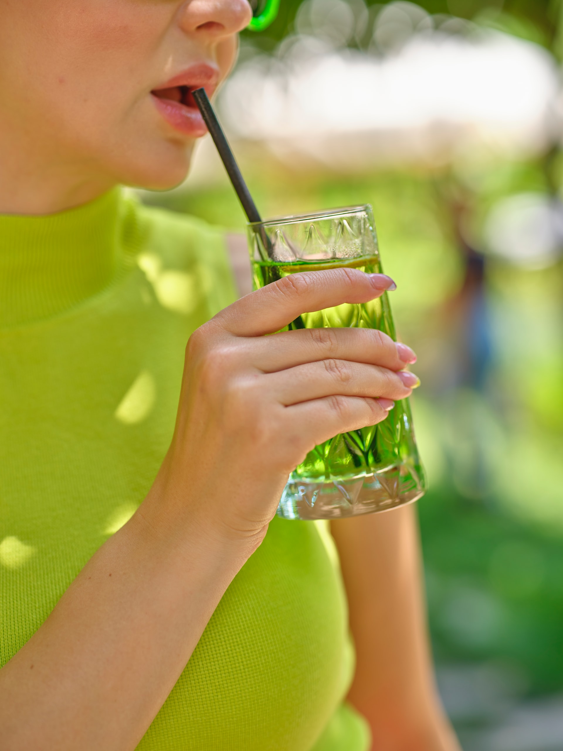 A woman wearing green drinking a green cocktail outside.