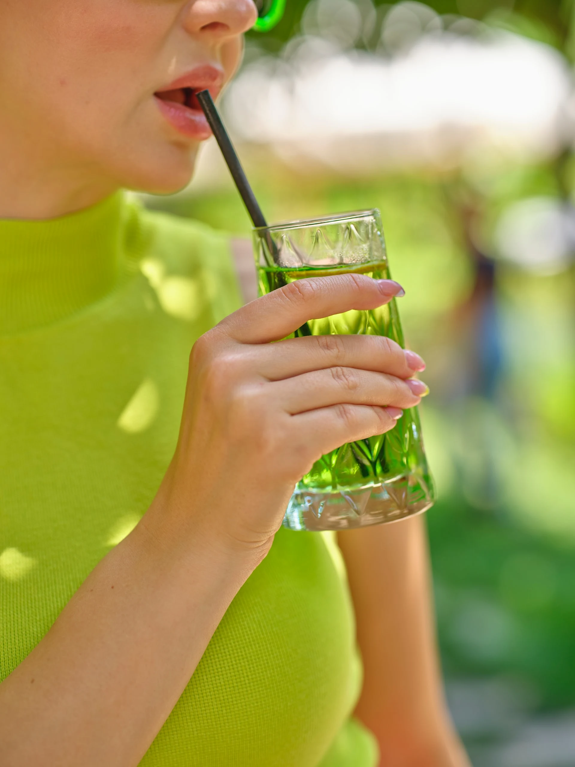 A woman wearing green drinking a green cocktail outside.