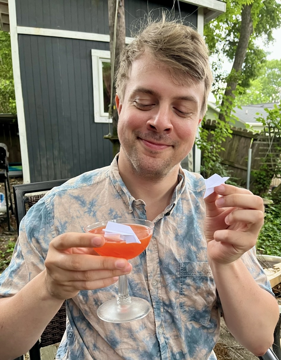 Ethan holding a paper plane cocktail with two actual paper planes outside.