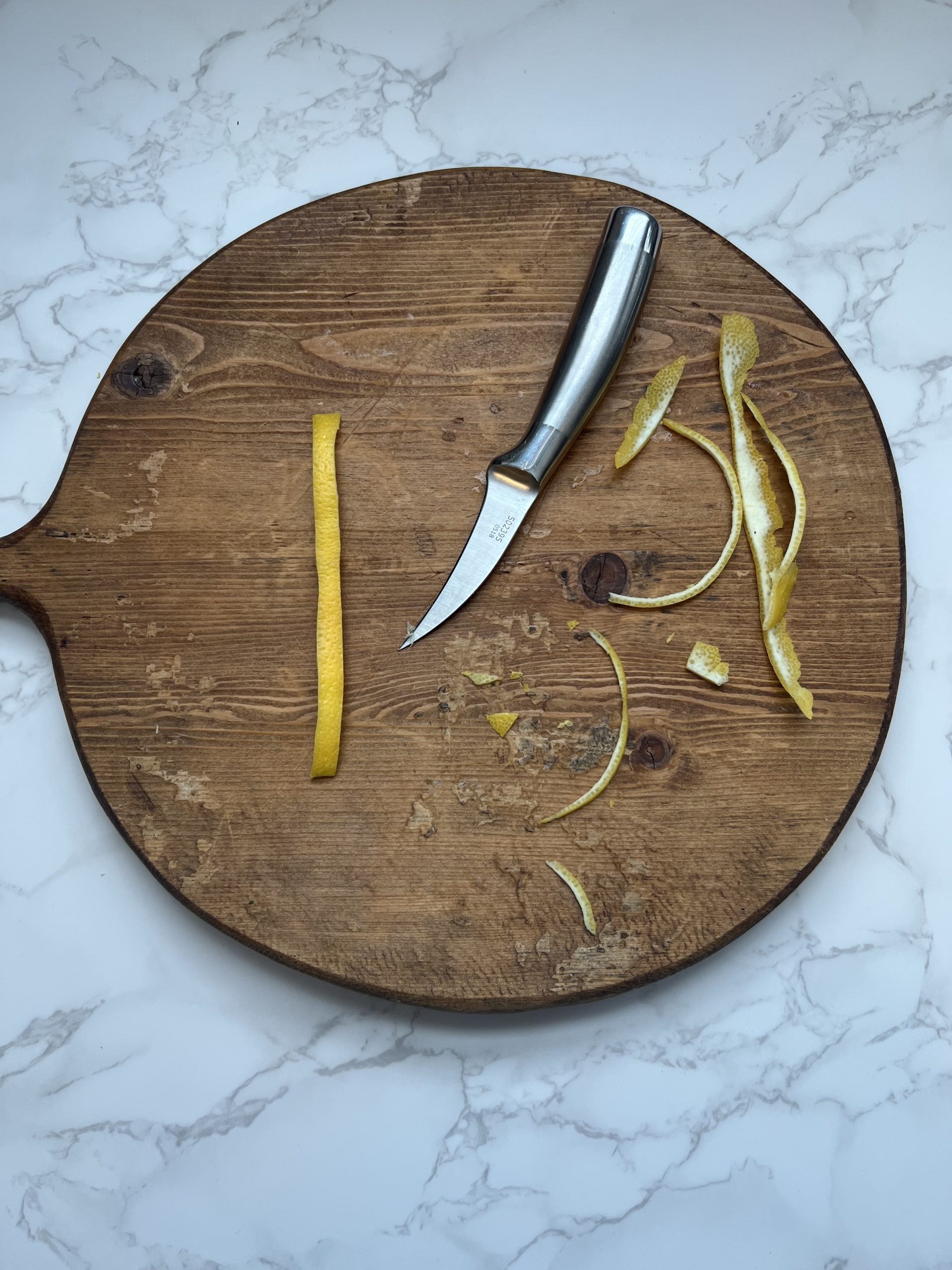 A uniform, trimmed lemon ribbon with a knife and trimmed off pieces of the lemon peel on a cutting board.