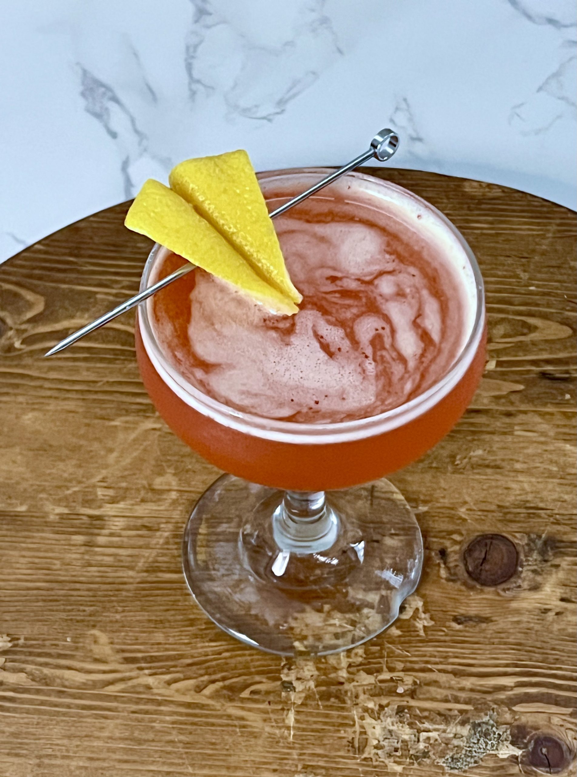 A close up of a paper plane garnish made out of a lemon peel on a vivid red Paper Plane cocktail.