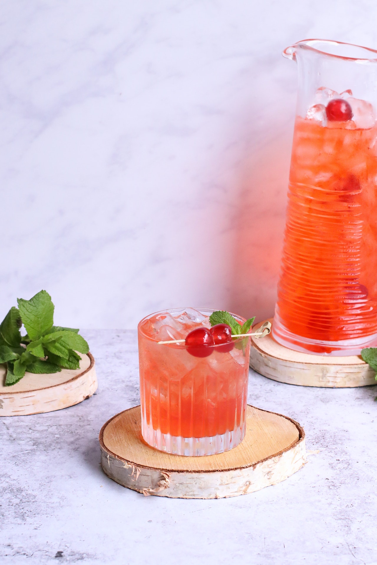 A tart cherry juice vodka cocktail in a glass and pitcher garnished with mint and cherries.