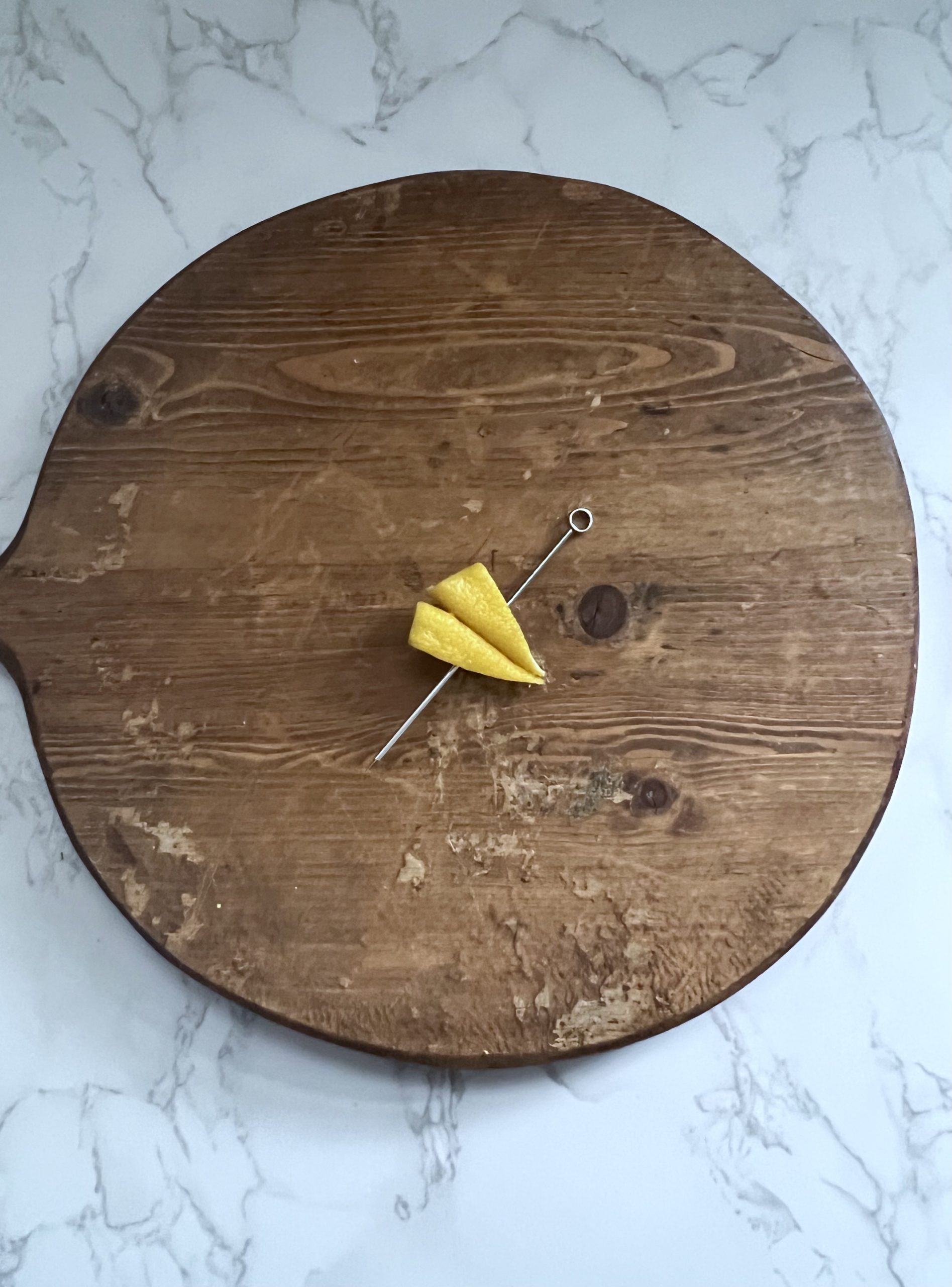 A paper plane made out of a lemon peel with a cocktail pick through it on a cutting board.
