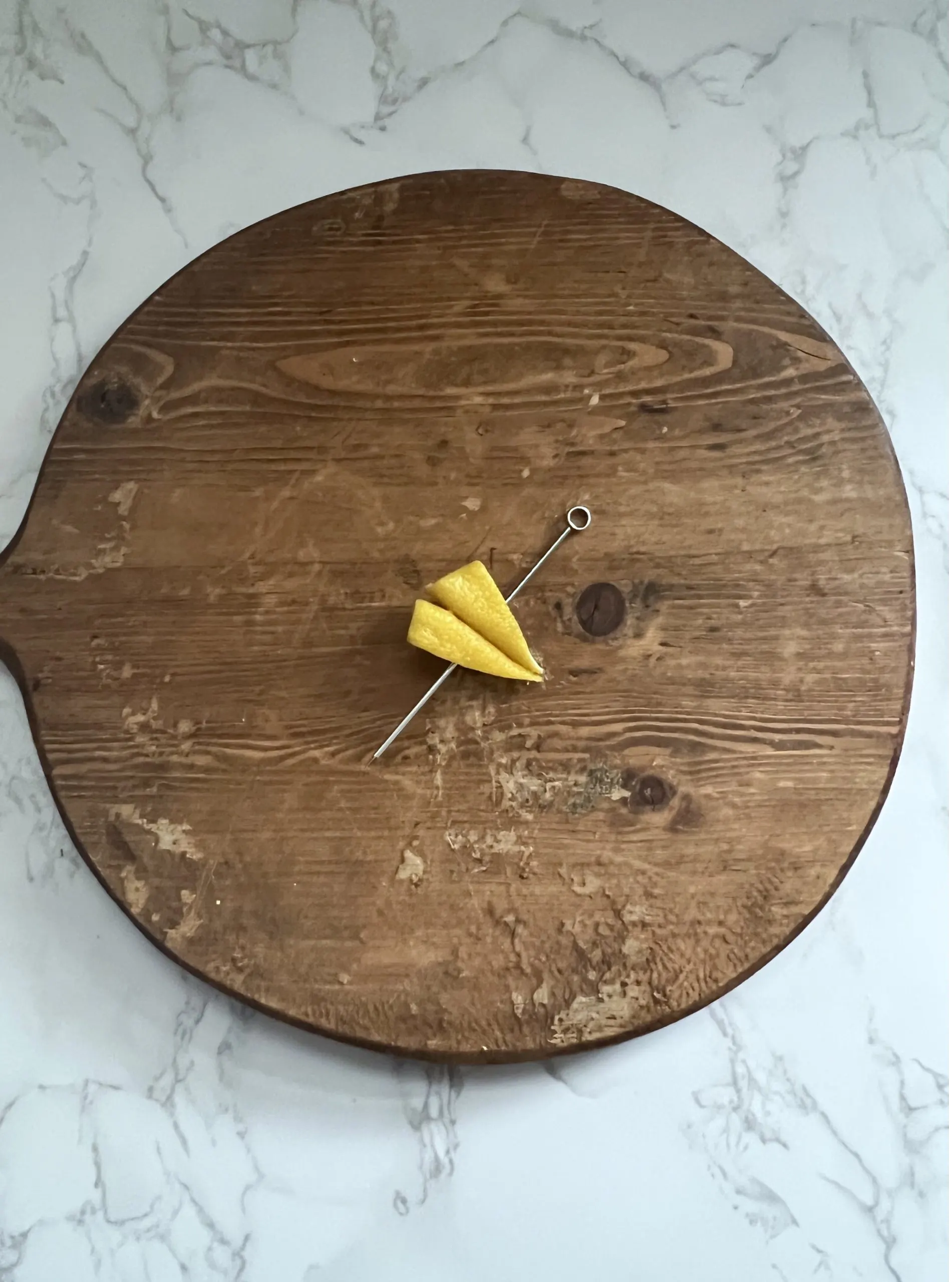 A lemon peel garnish shaped like a paper plane with a cocktail pick through it.