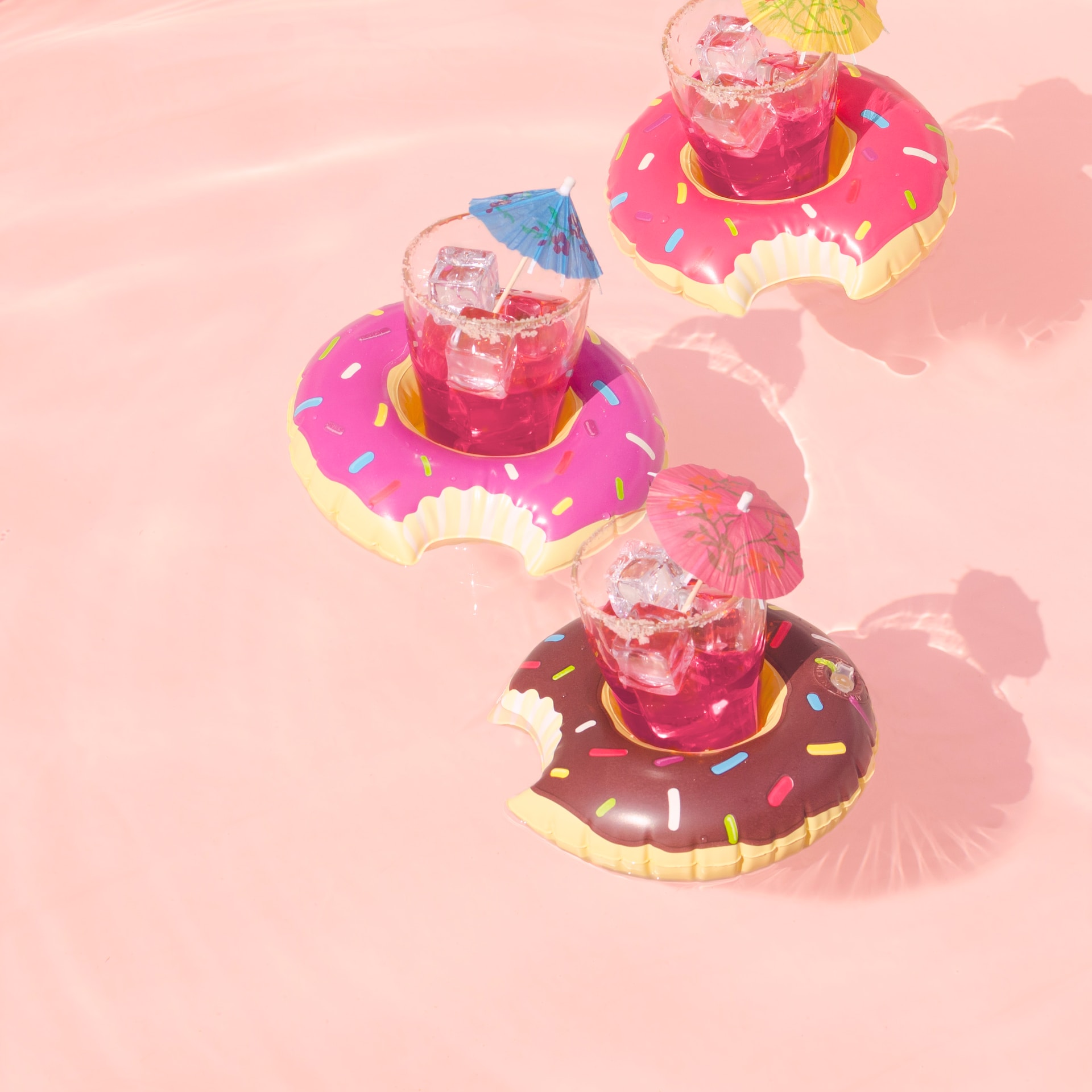 A fun image of bright pink rosé cocktails floating in donut-shaped floats in a light pink pool.