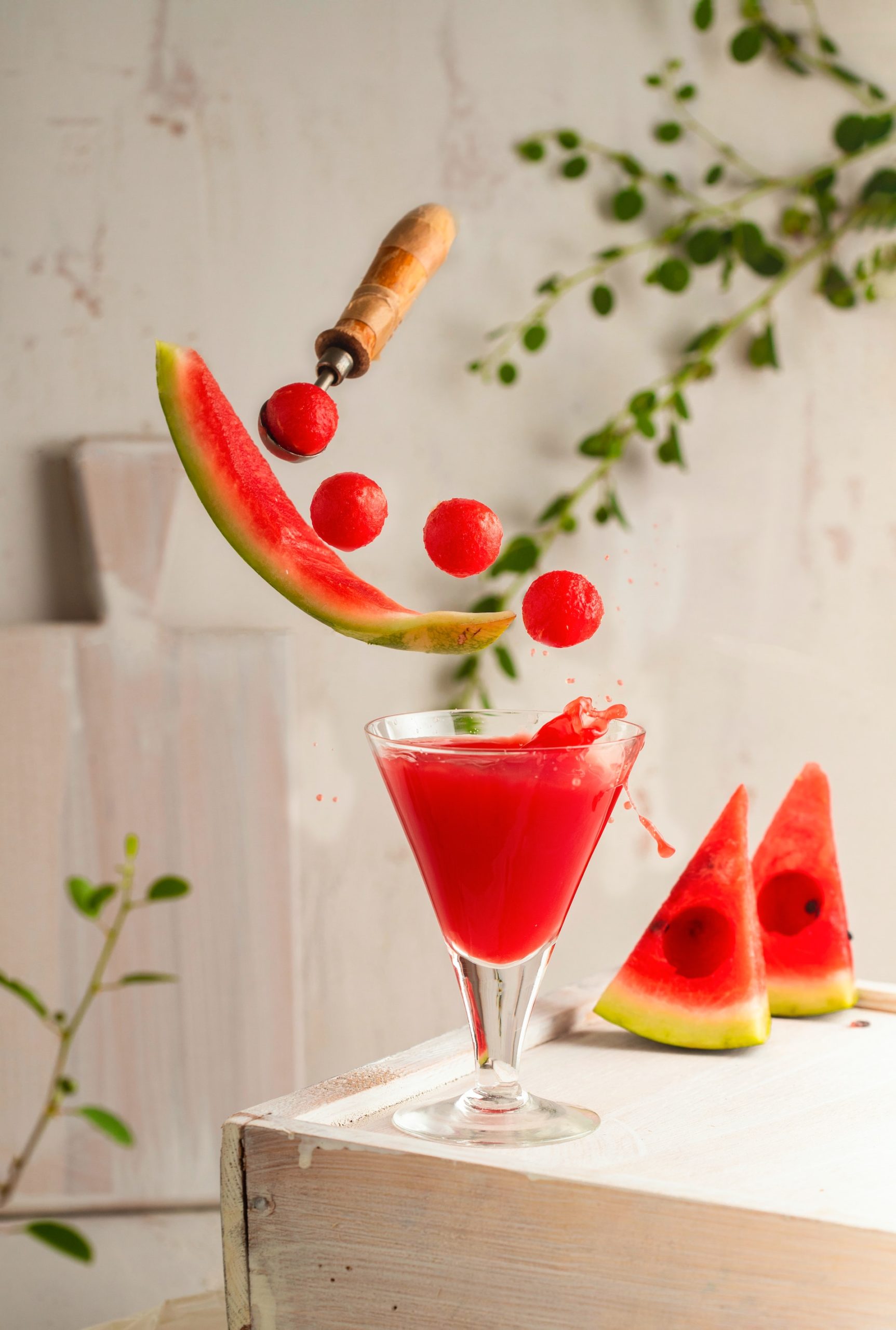 A fun image of a melon baller floating in midair and scooping balls of watermelon into a watermelon cocktail.