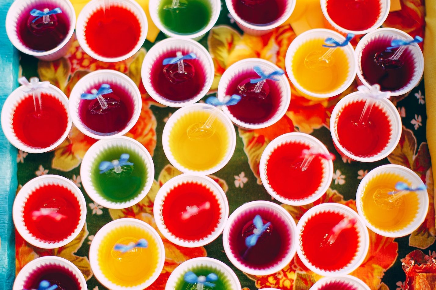 Colorful jello shots in white ceramic cups on a floral table cloth.