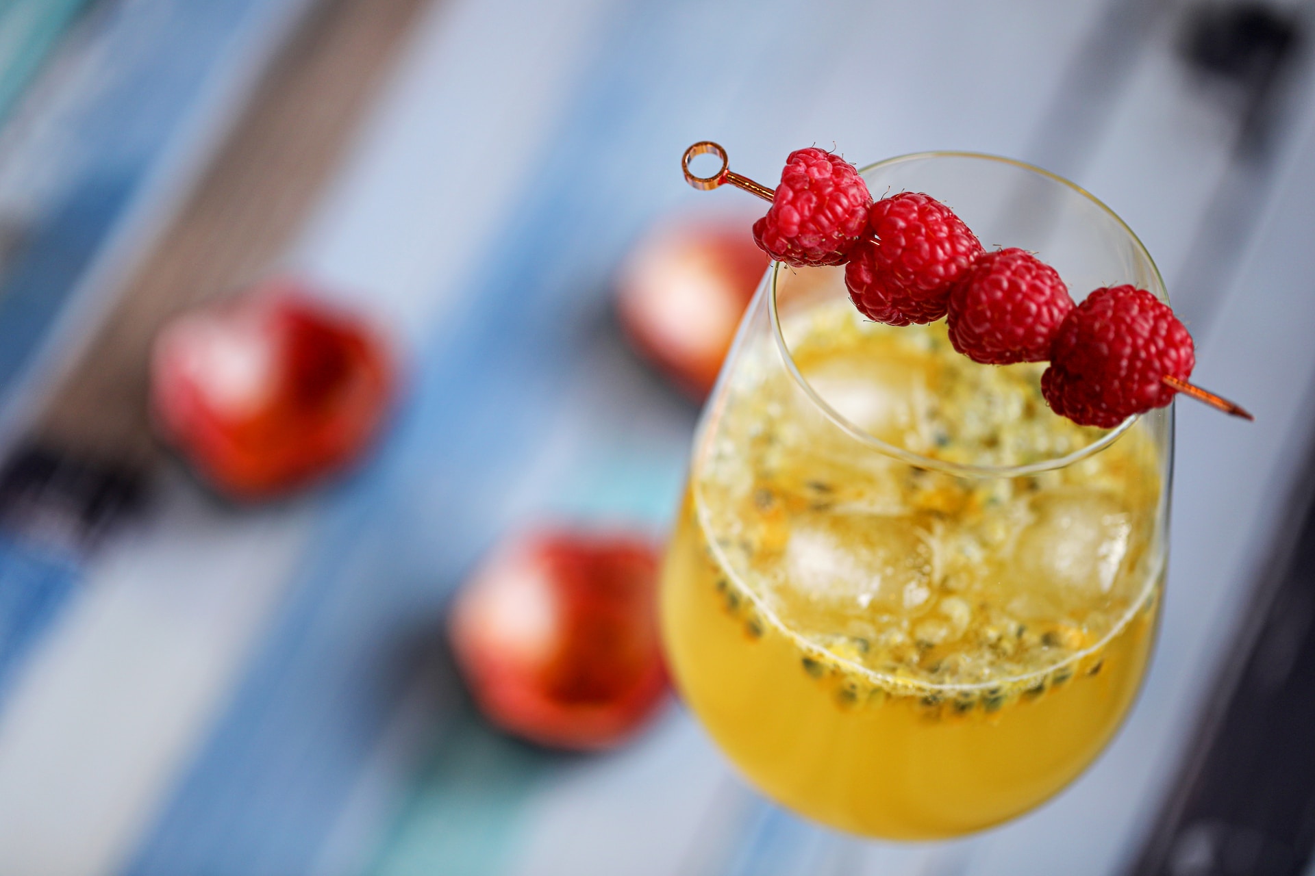 A yellow passionfruit vodka cocktail on a table garnished with raspberries on a cocktail pick