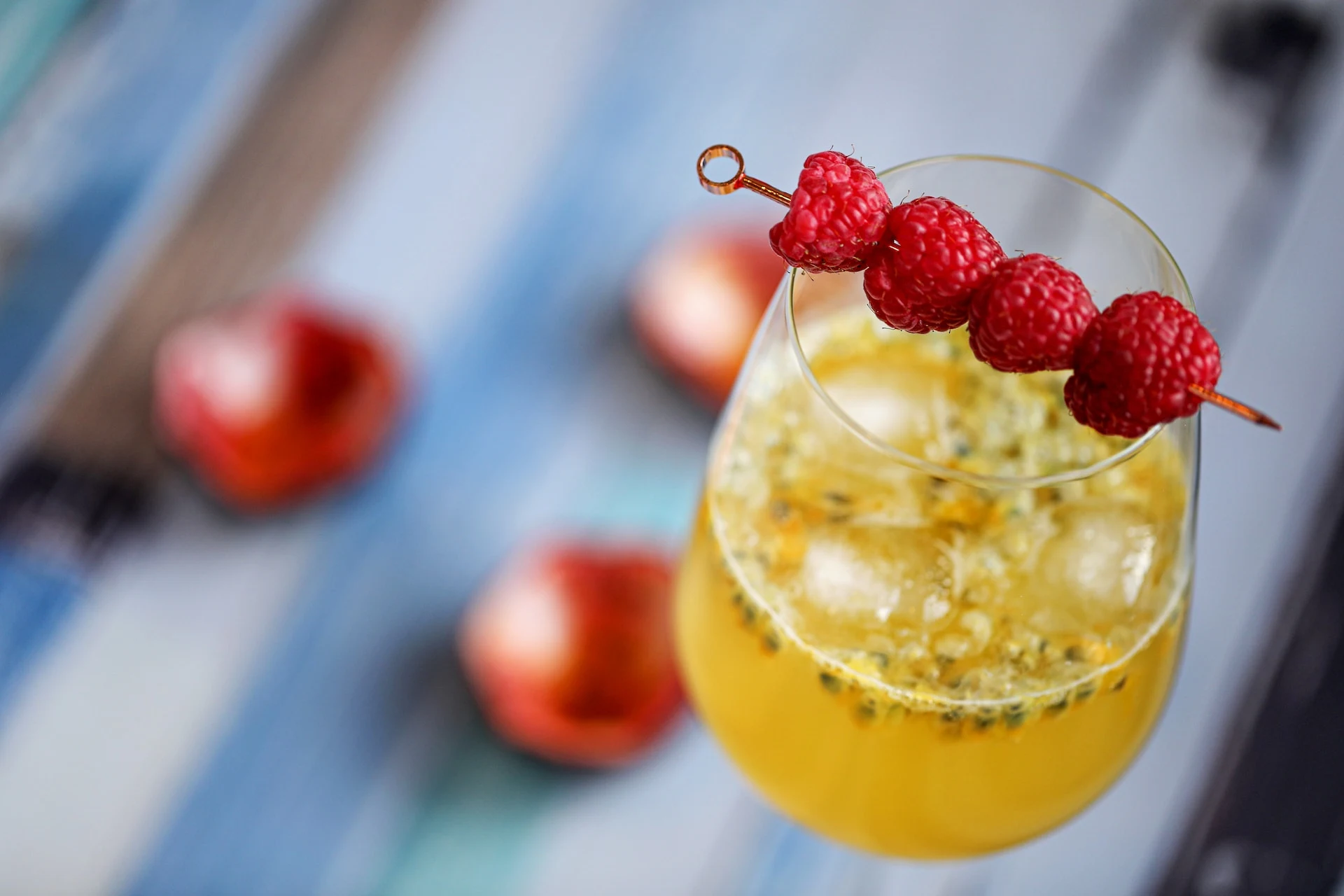 A yellow passionfruit vodka cocktail on a table garnished with raspberries on a cocktail pick